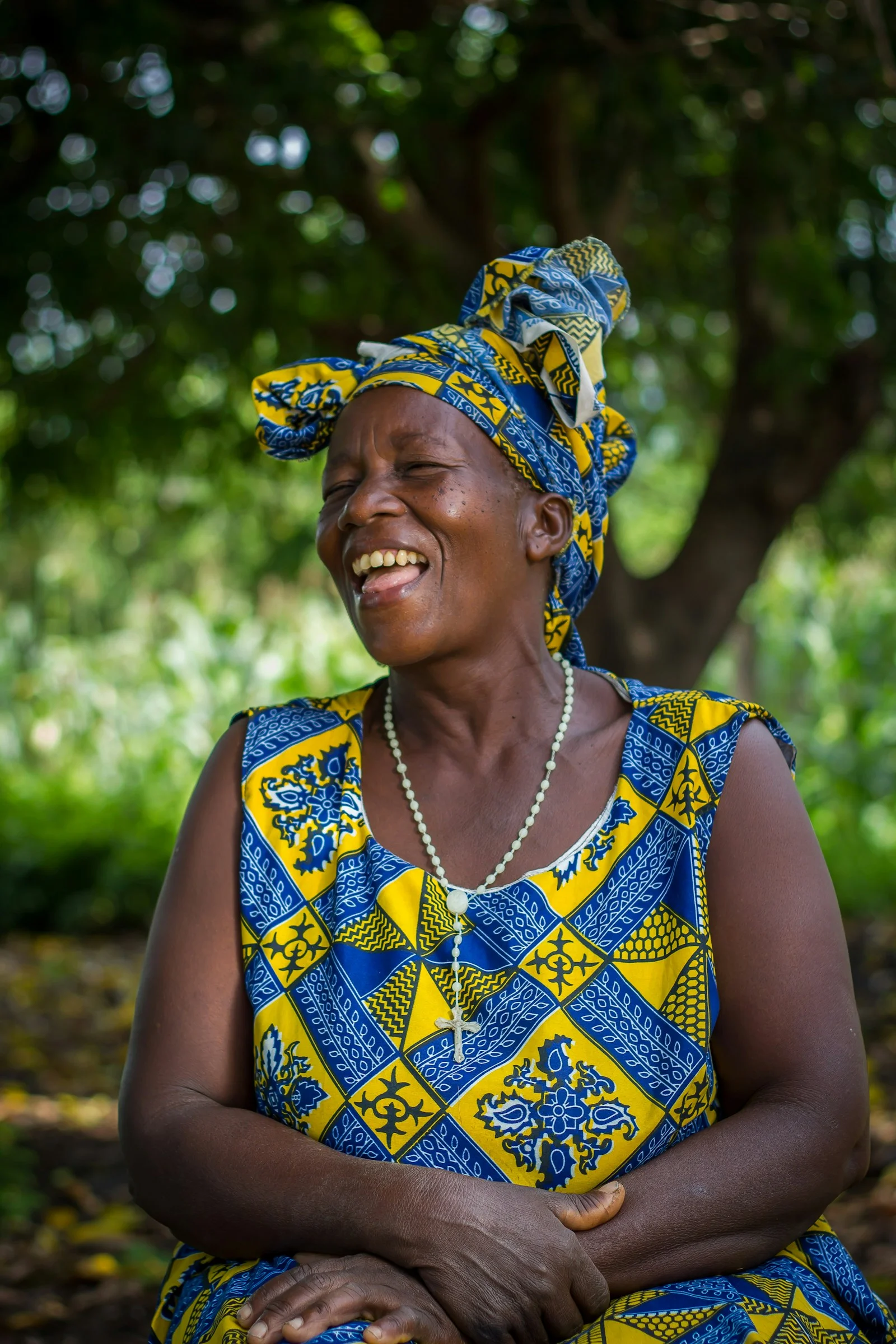A woman wearing a patterned yellow and blue headwrap and dress with a rosary