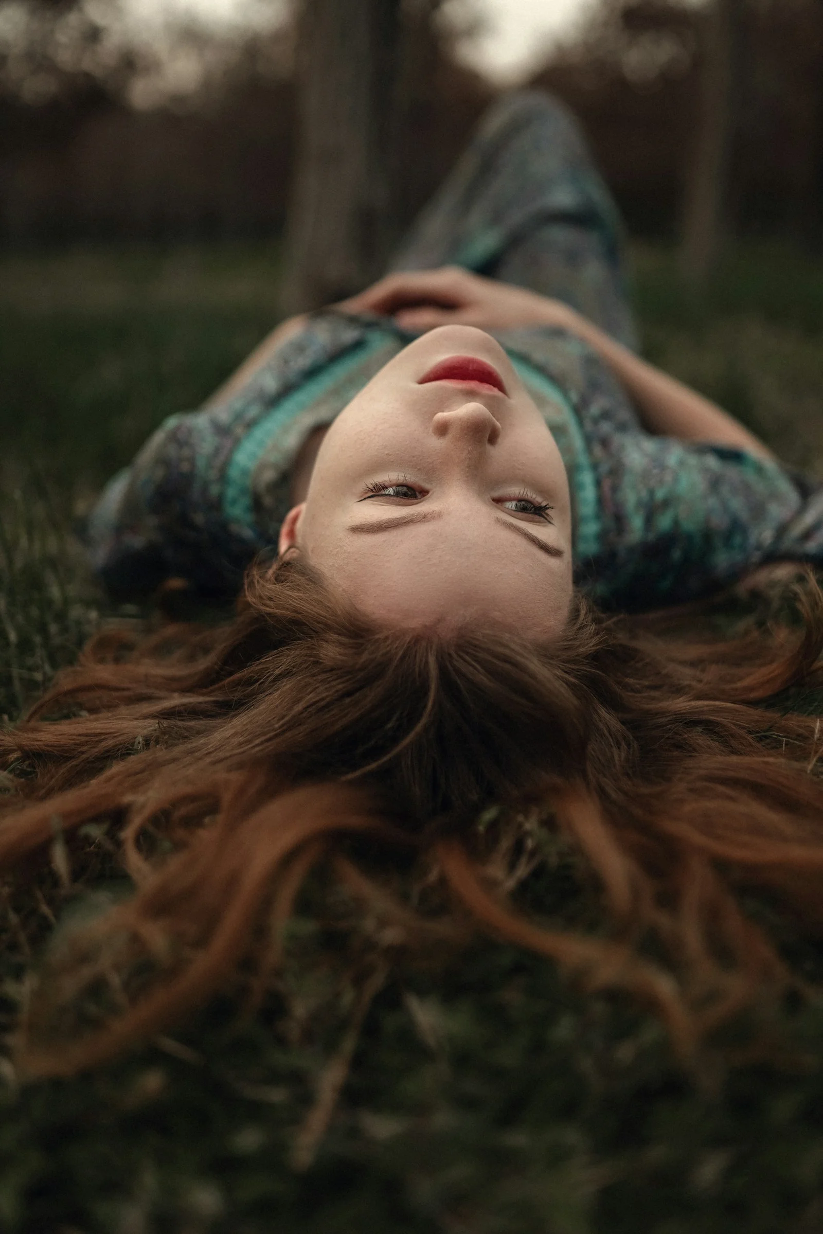 a young girl laying on the grass with her hair blowing in the wind
