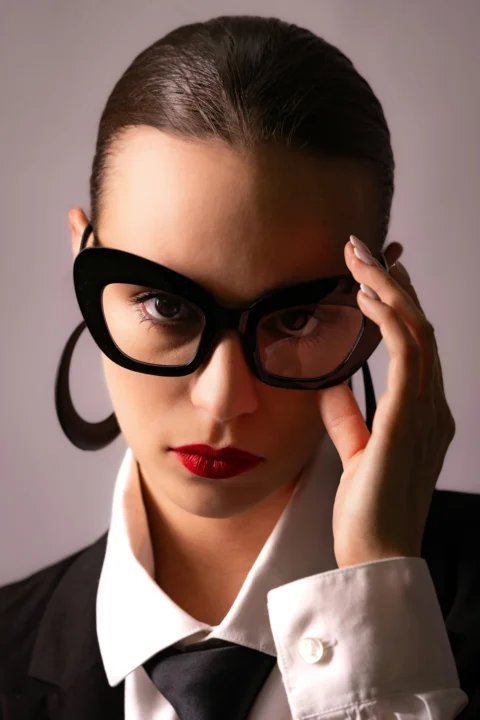 Elegant woman with large glasses looks directly at the camera