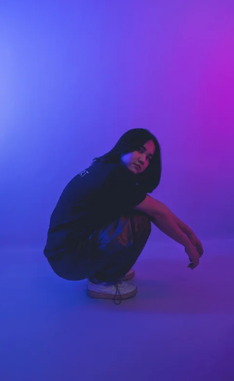 a woman squatting on a skateboard in front of a purple and blue background