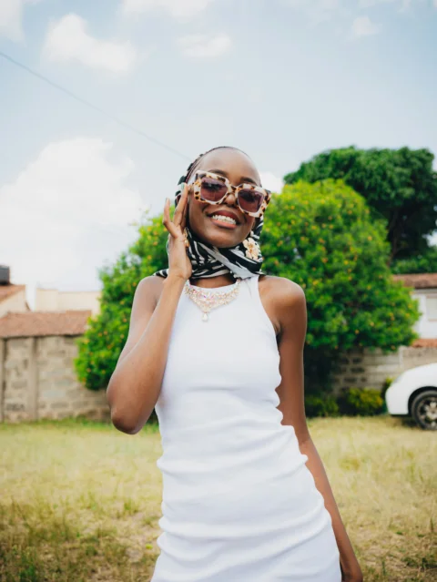 A young woman smiles, wearing sunglasses and a headscarf