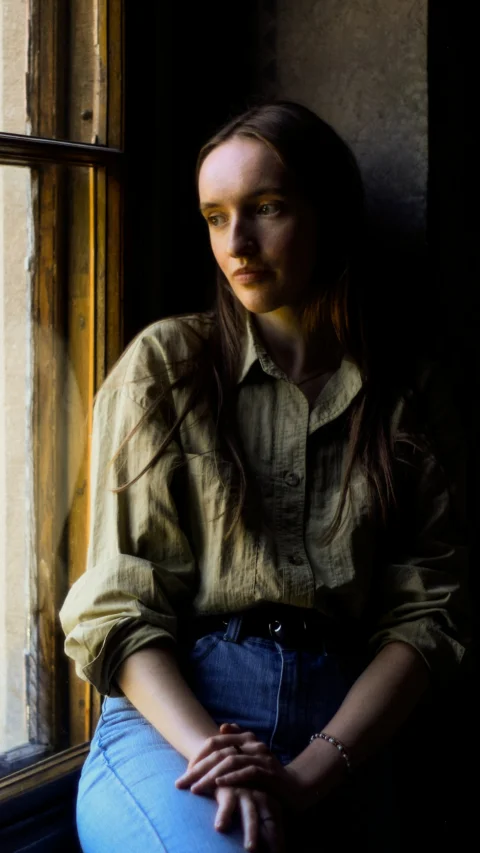 A woman sitting on a window sill looking out the window