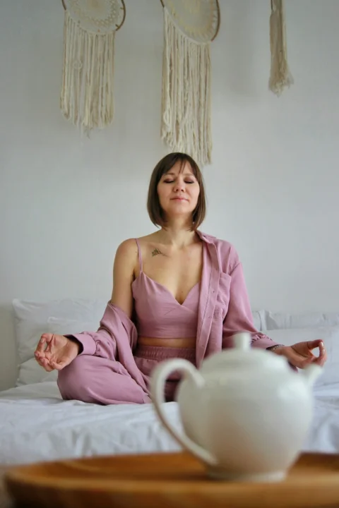 a woman sitting on a bed with a teapot in front of her