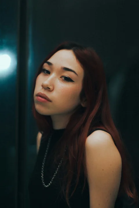 一名留著紅色長髮的女子站在鏡子前