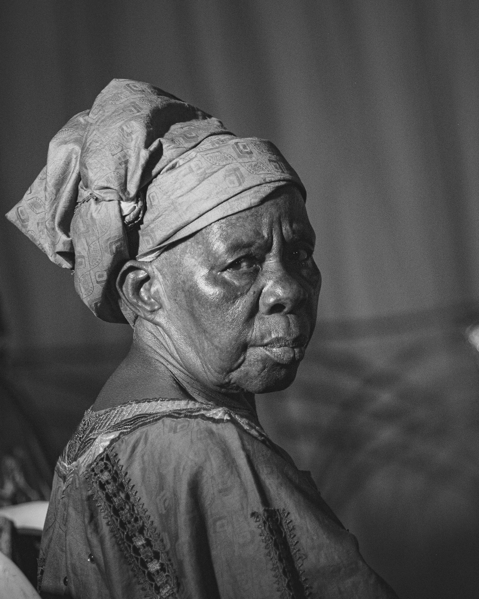 An older woman wearing a patterned headwrap and a textured garment in profile