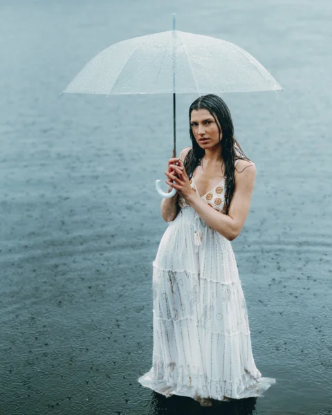 Woman stands in rain under umbrella