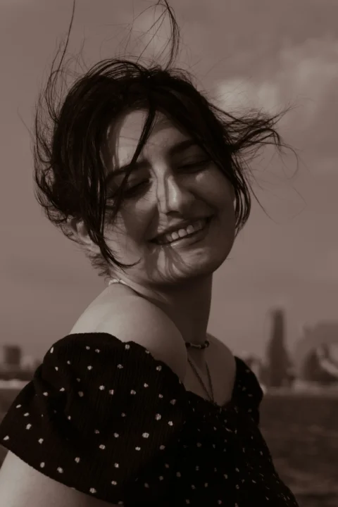 A smiling woman with windblown hair wearing a dark polka dot top