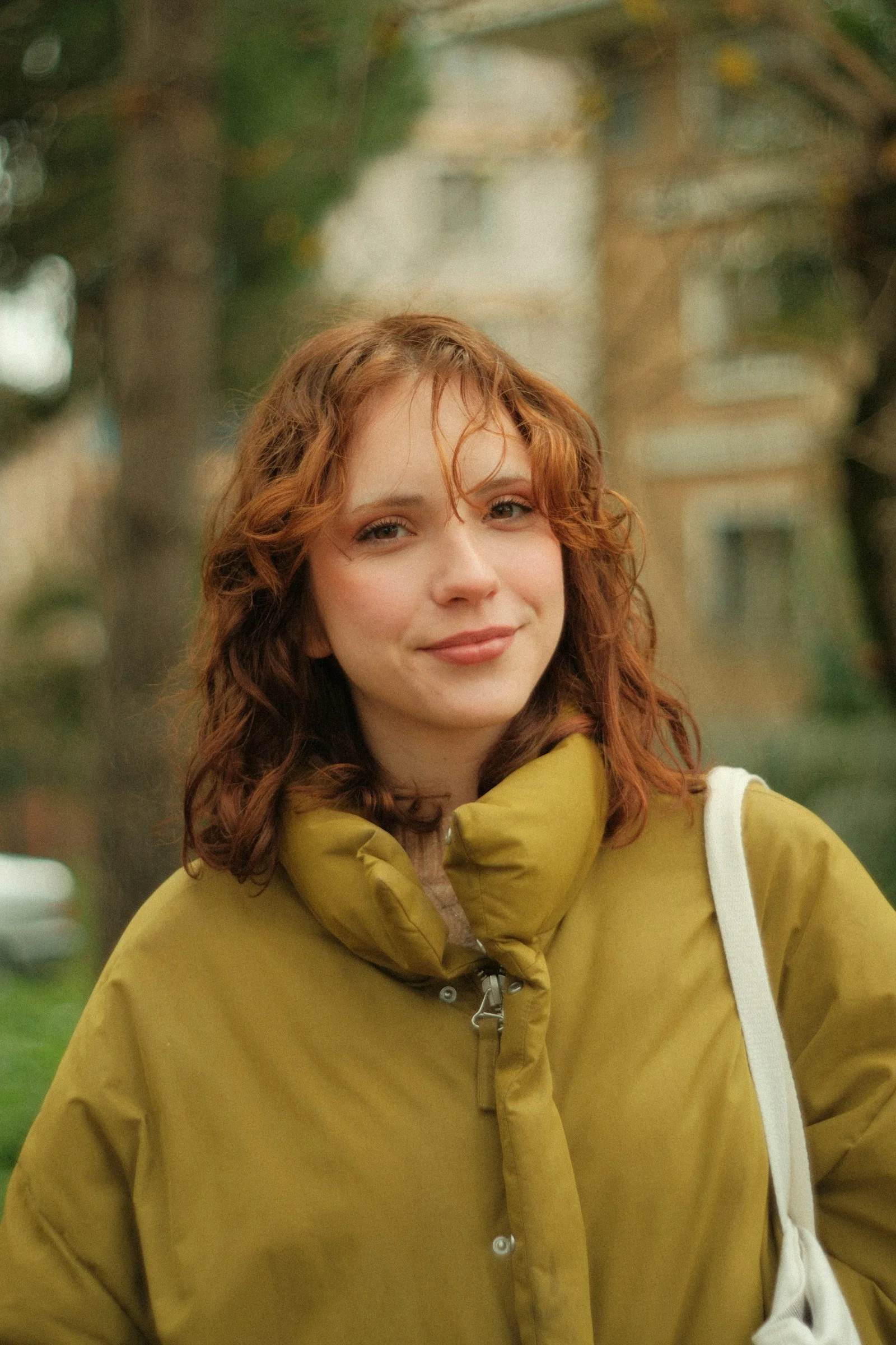 A woman with red hair is standing in a park