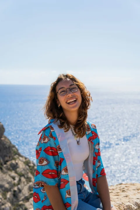 a woman sitting on top of a rock near the ocean