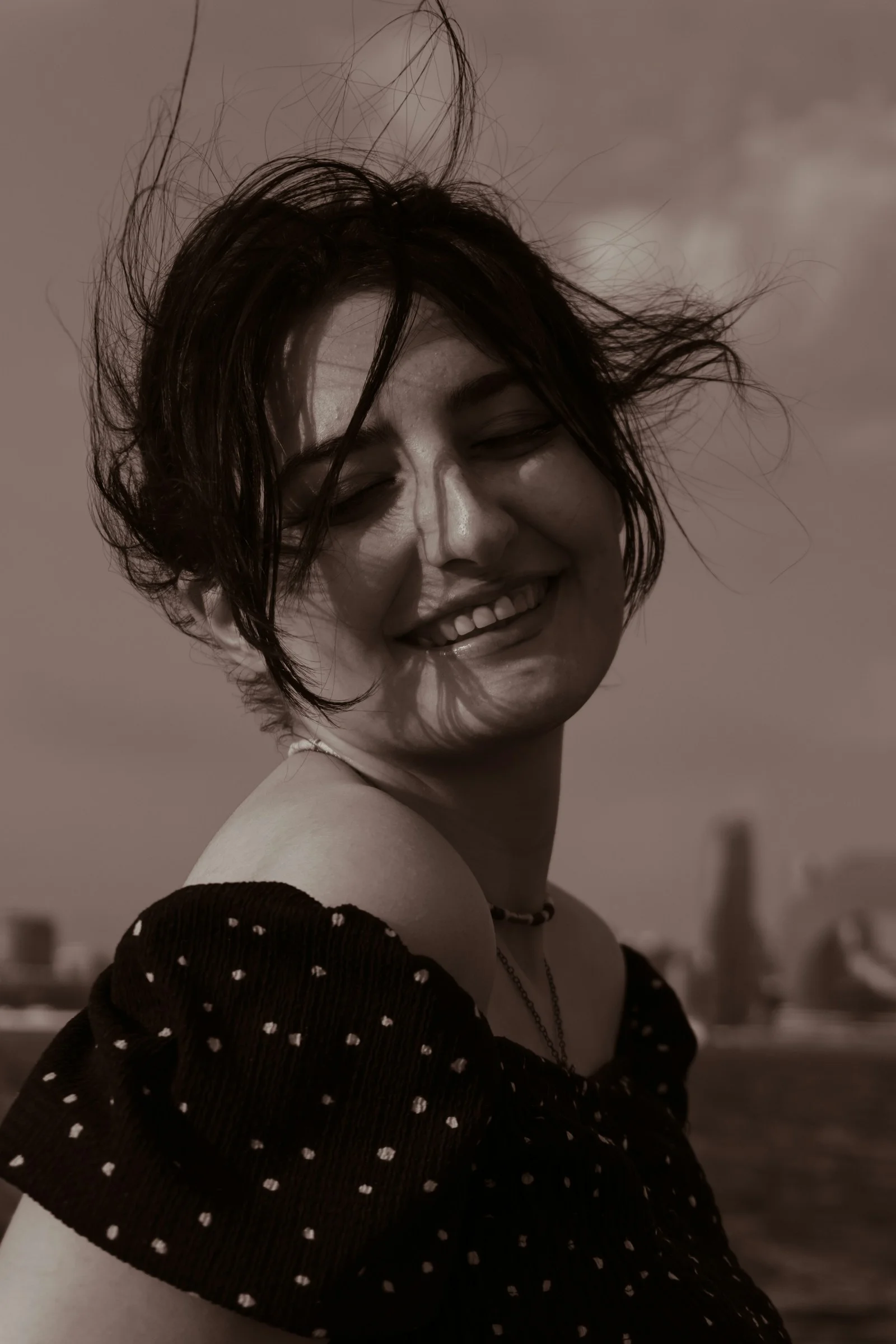 A smiling woman with windblown hair wearing a dark polka dot top