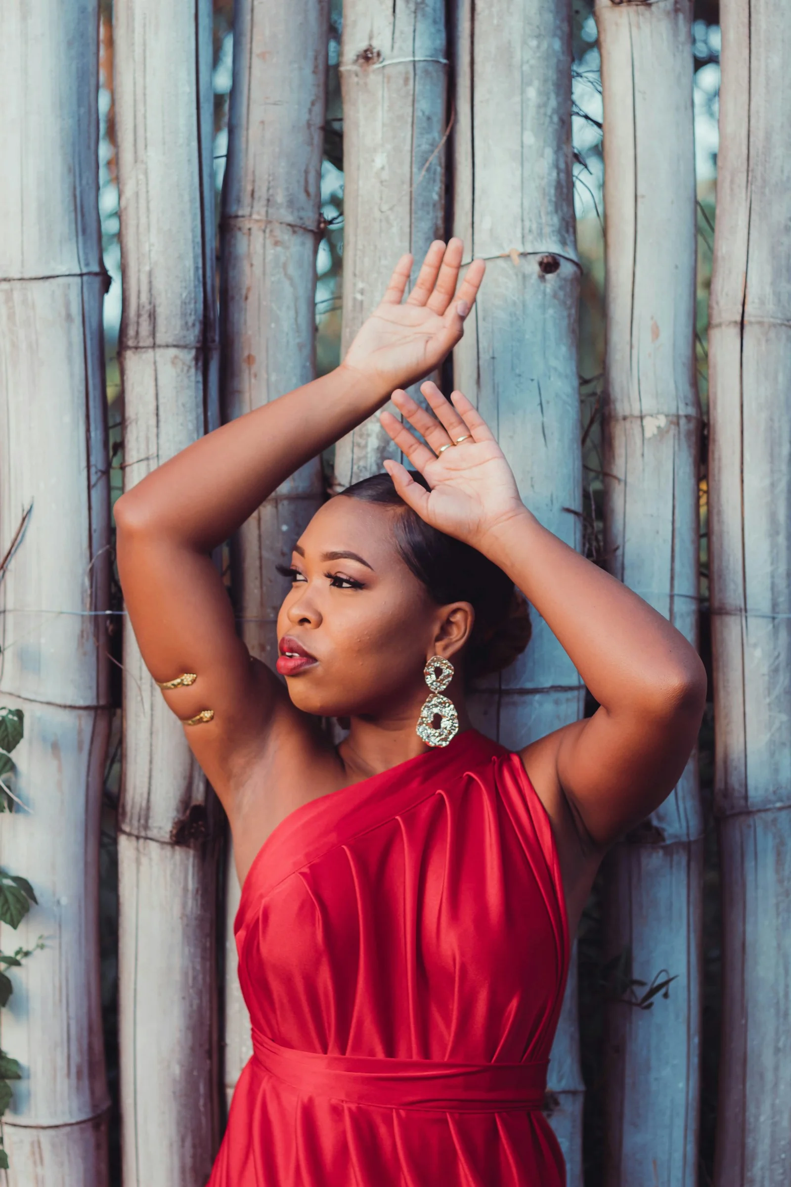 a woman in a red dress leaning against a bamboo fence