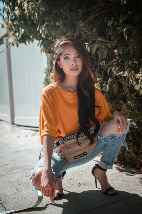 woman in orange crew neck t-shirt and blue denim jeans sitting on concrete floor