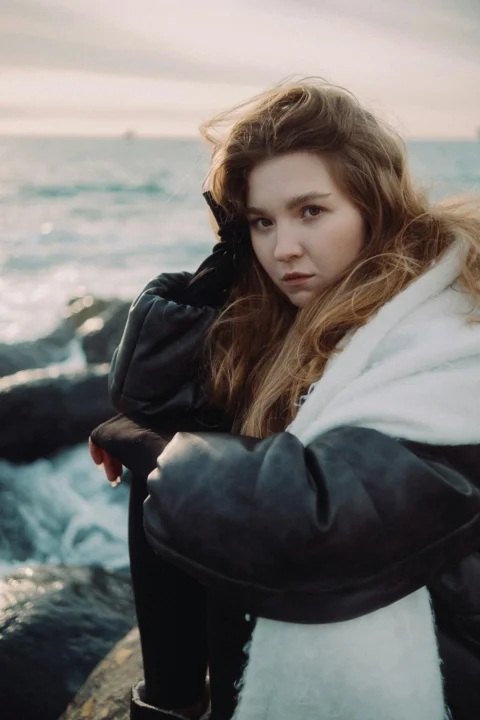 Woman poses by the ocean, looking at the camera