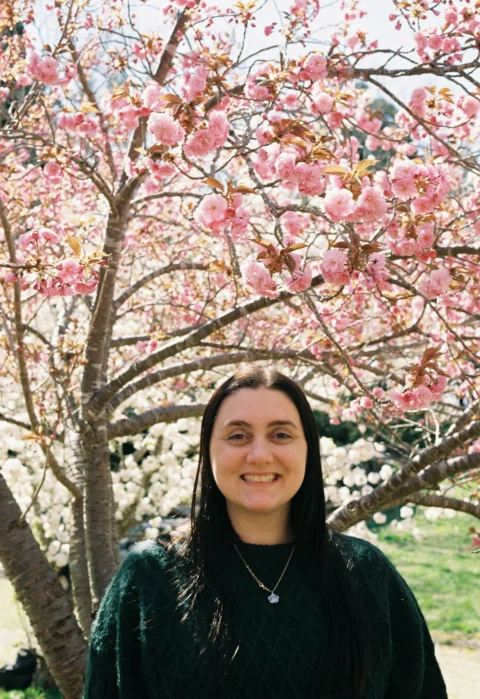 Woman smiling in front of a blooming cherry blossom tree