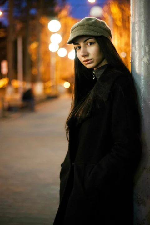身穿黑色大衣站在墙边的女子