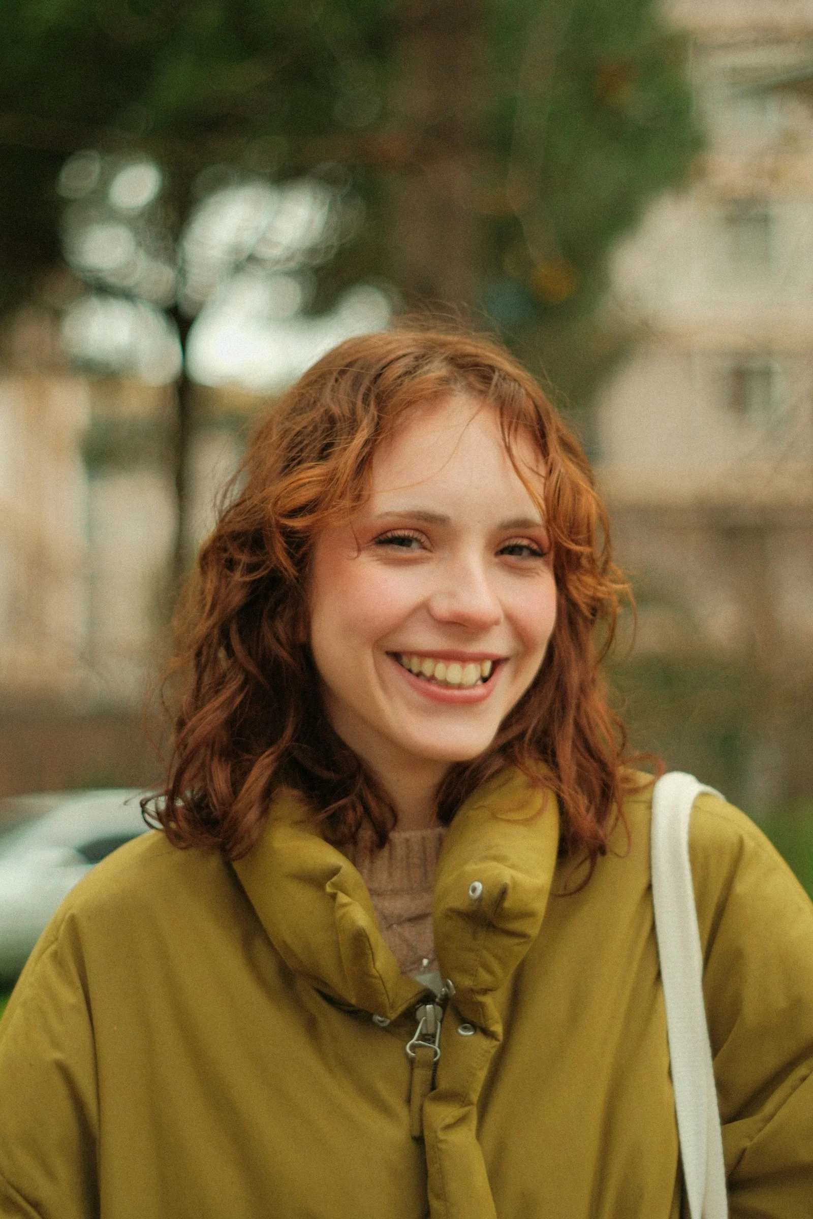 A woman with red hair is smiling and holding a white bag