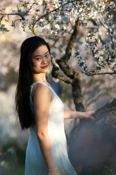 Young woman in white dress near blooming tree