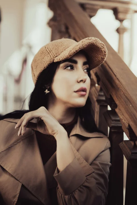 A woman in a brown coat and hat leaning against a railing