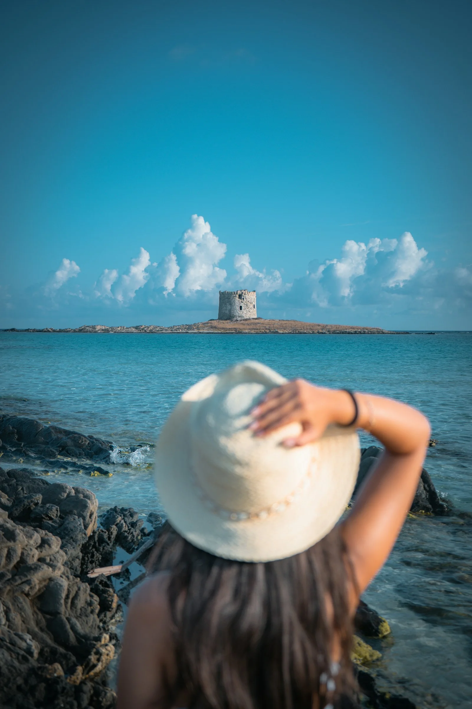 Woman in hat looks at island tower by the sea