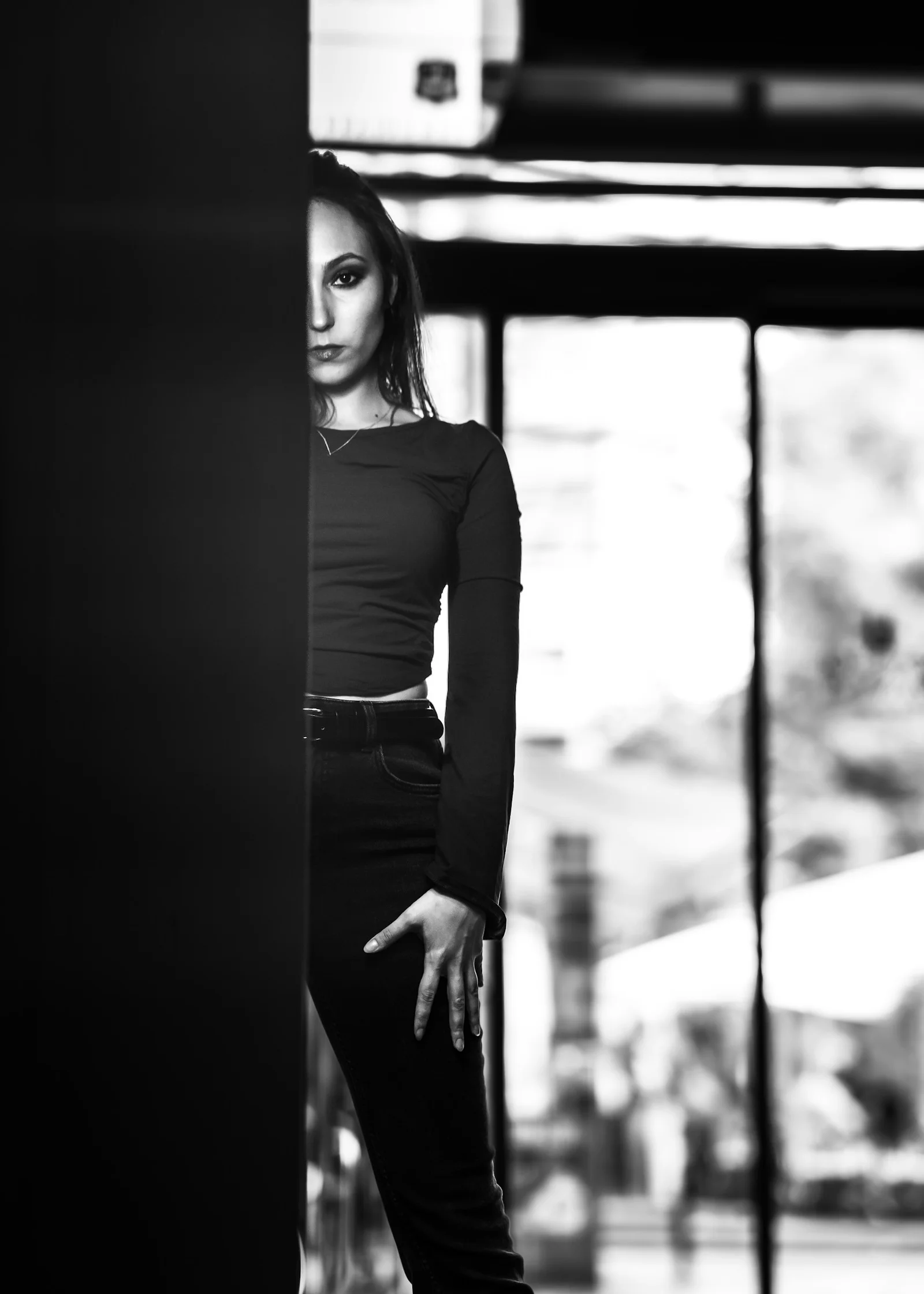 A woman in a long-sleeved top and jeans partially obscured by a dark pillar