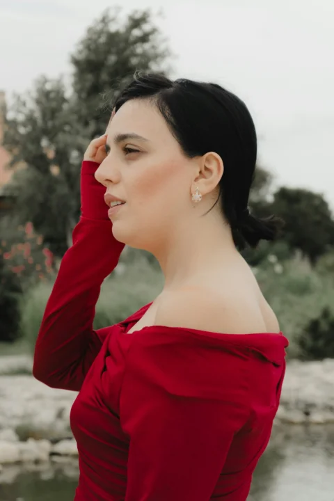 A woman in a red off-the-shoulder top touching her hair outdoors