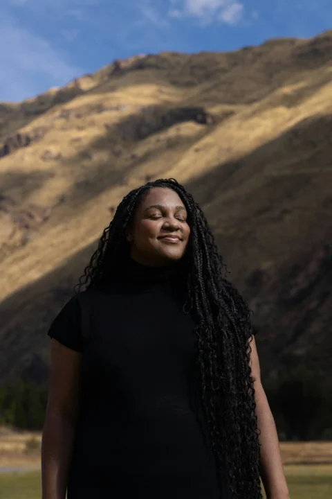 Woman smiles with eyes closed near a mountain