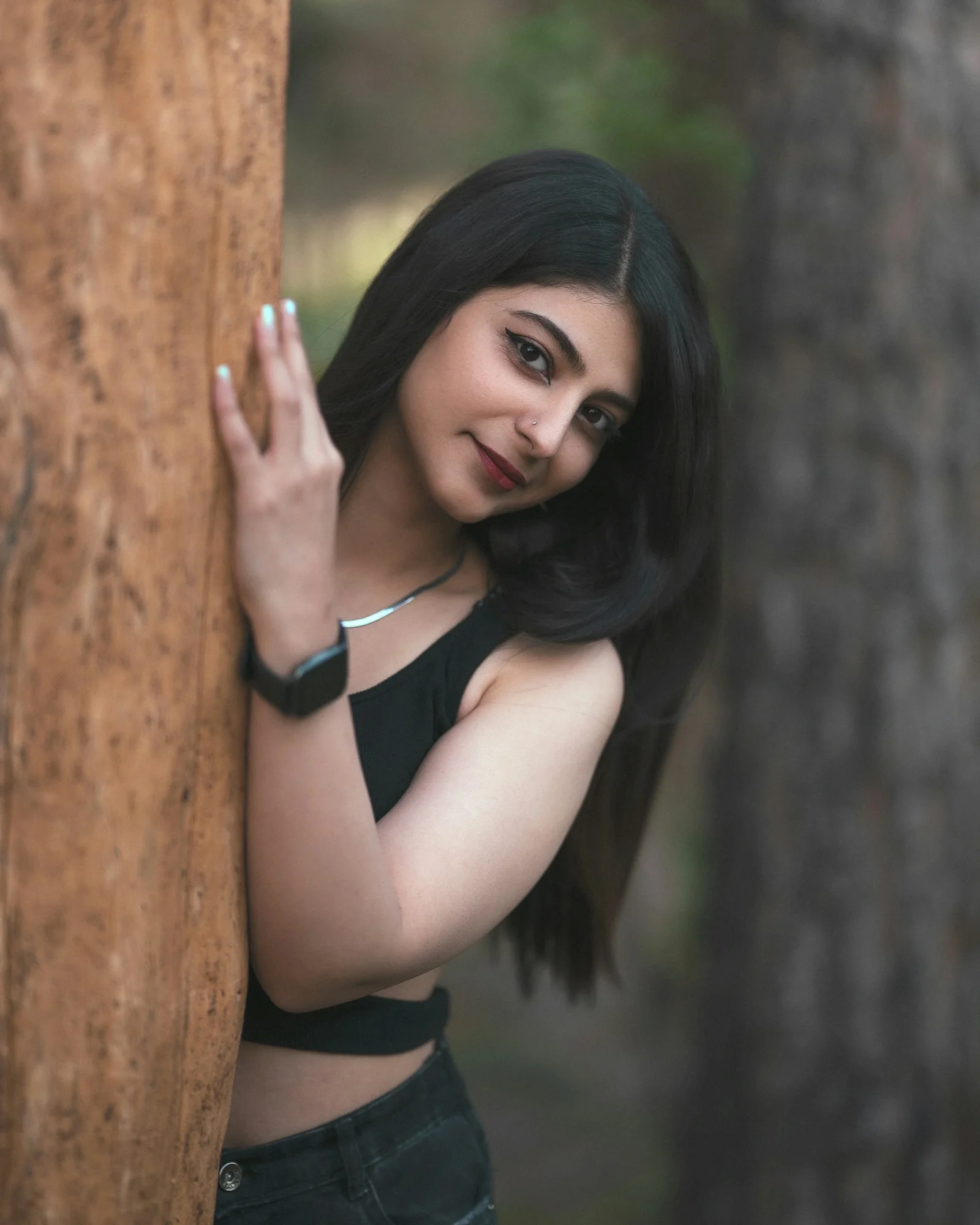 A woman in a black top leaning against a tree trunk in a forest