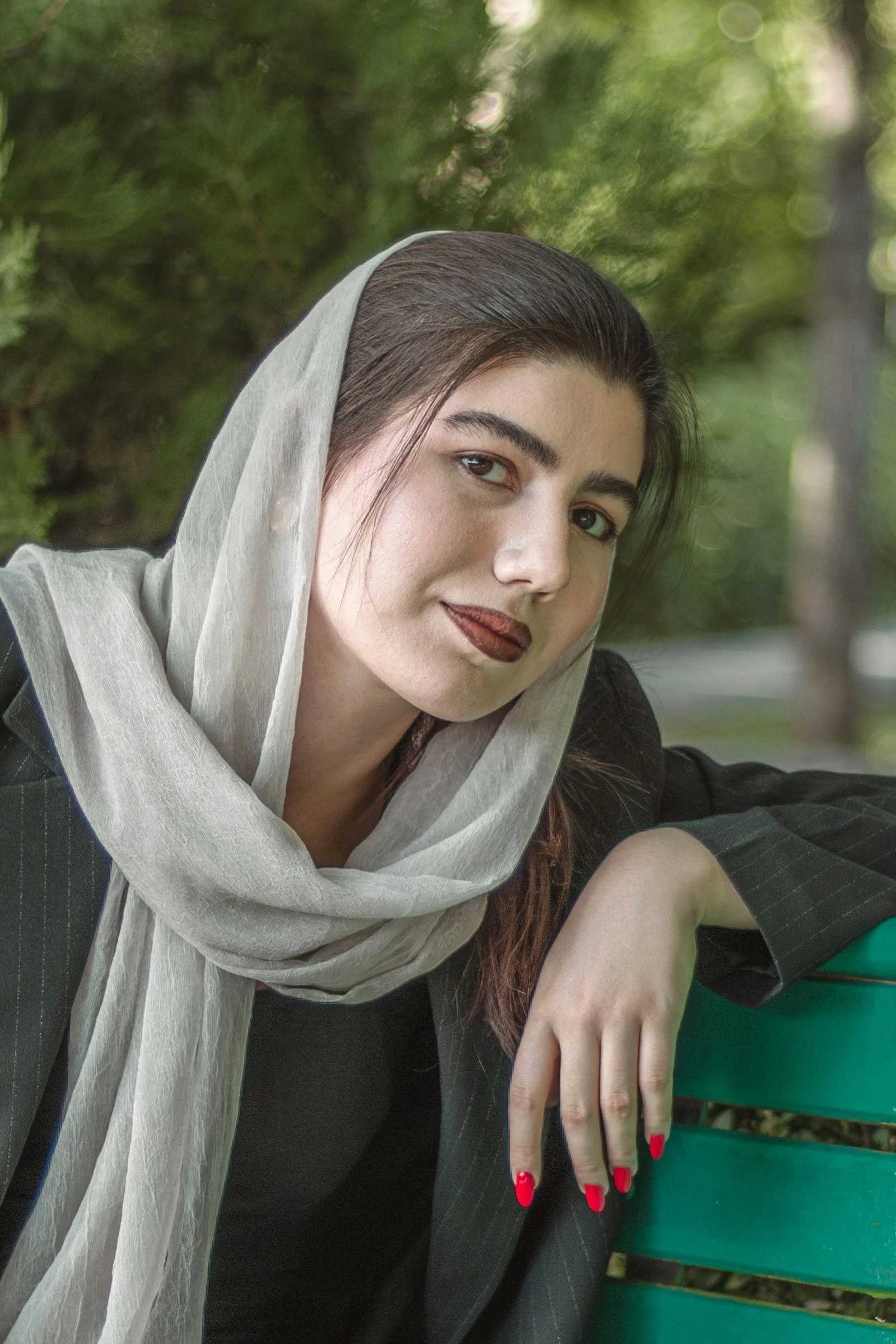 A young woman wearing a headscarf sits on a bench