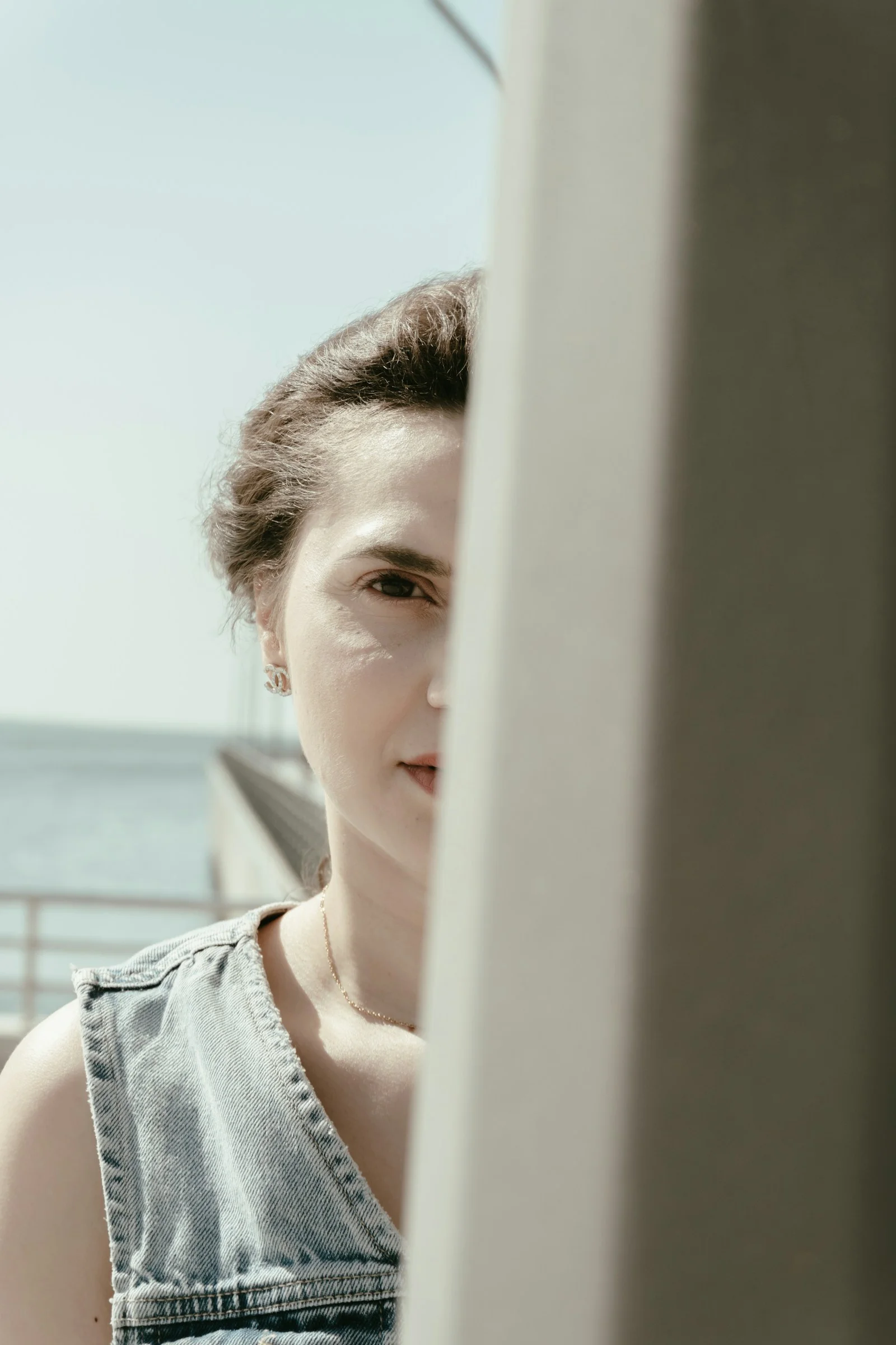 A woman's face partially hidden by a pillar outdoors