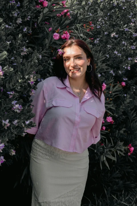 A woman in a pink button-down shirt standing before a flowering oleander bush
