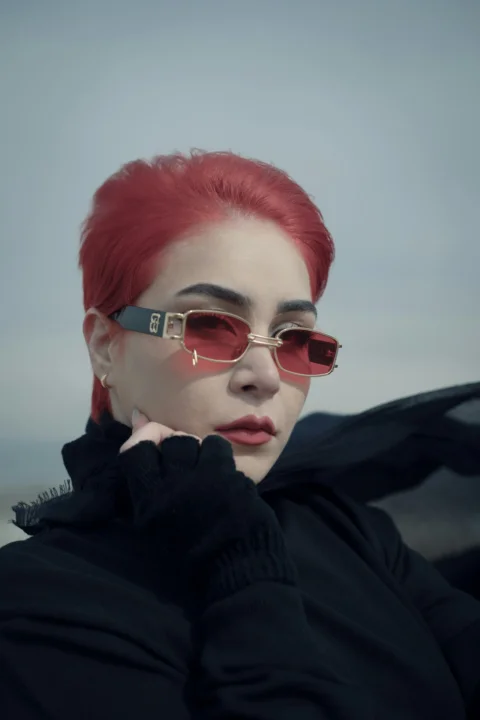 一位紅髮女性戴著太陽眼鏡，身穿黑色夾克