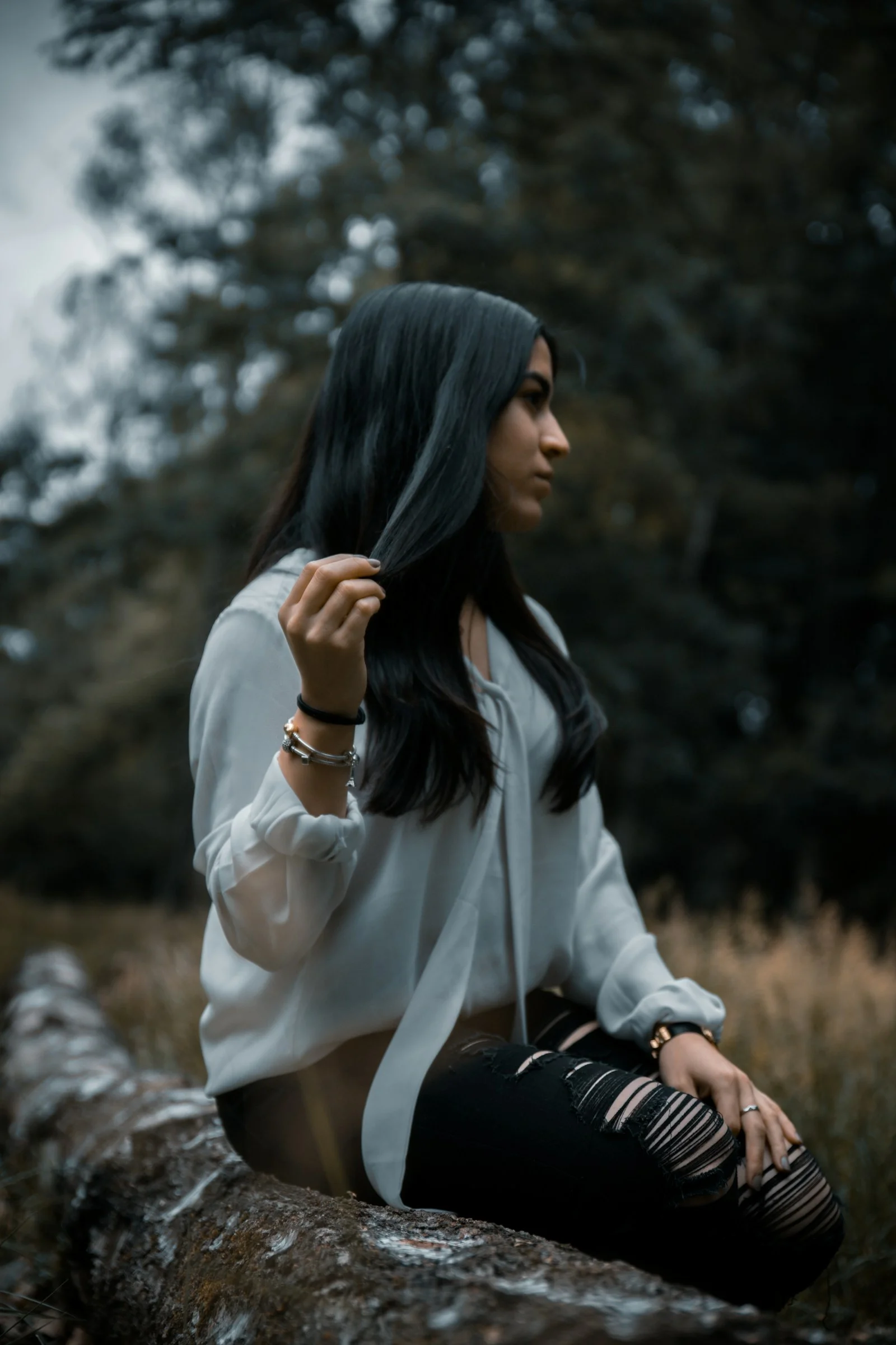 woman in white long sleeve shirt and black pants sitting on rock during daytime