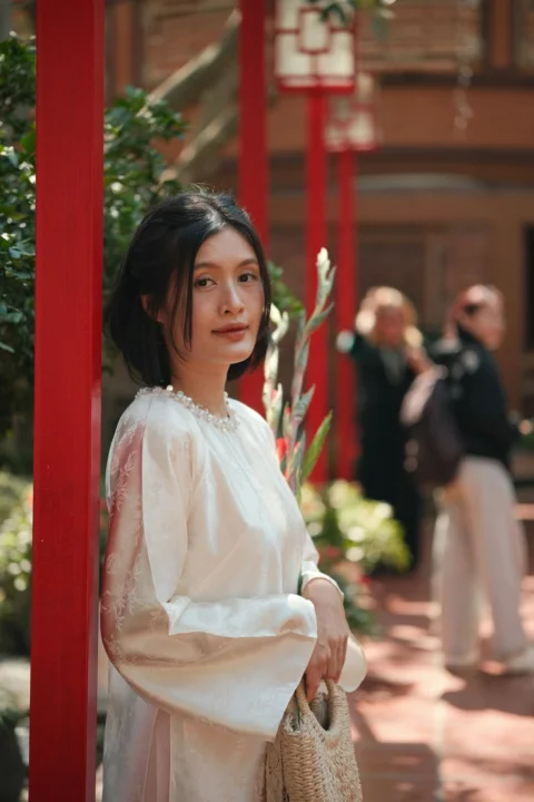 A woman in a white dress stands near red pillars