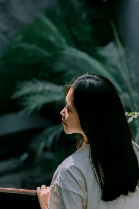 A woman standing next to a window with a plant behind her