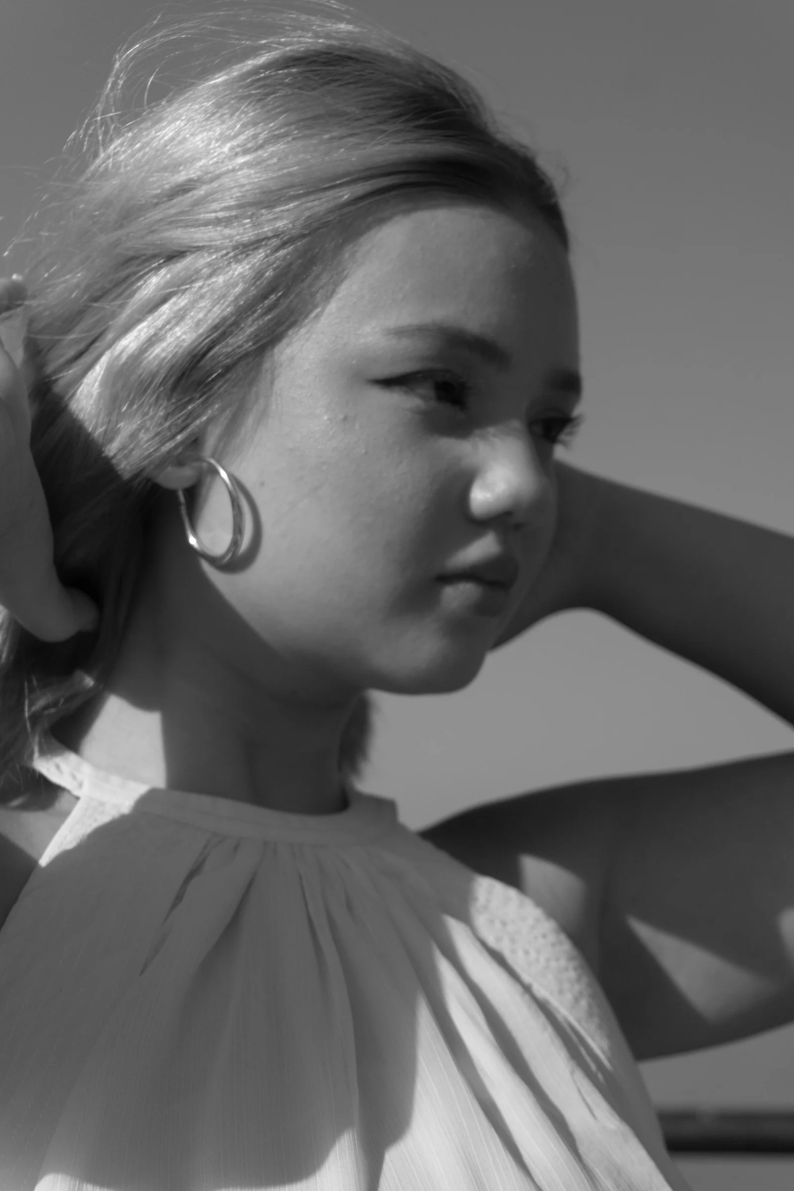 A young woman with hoop earrings adjusting her hair in black and white