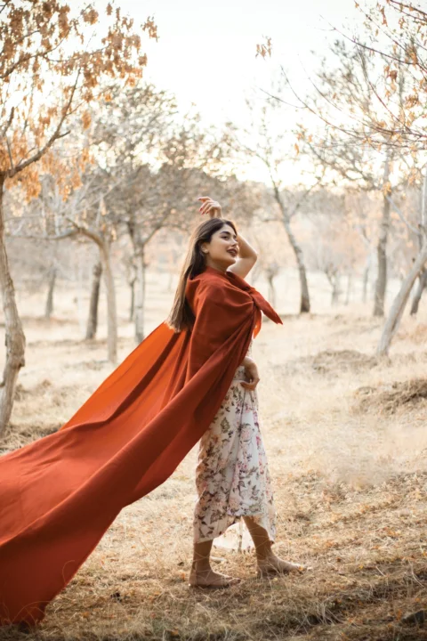 a woman in a red cape is standing in a field