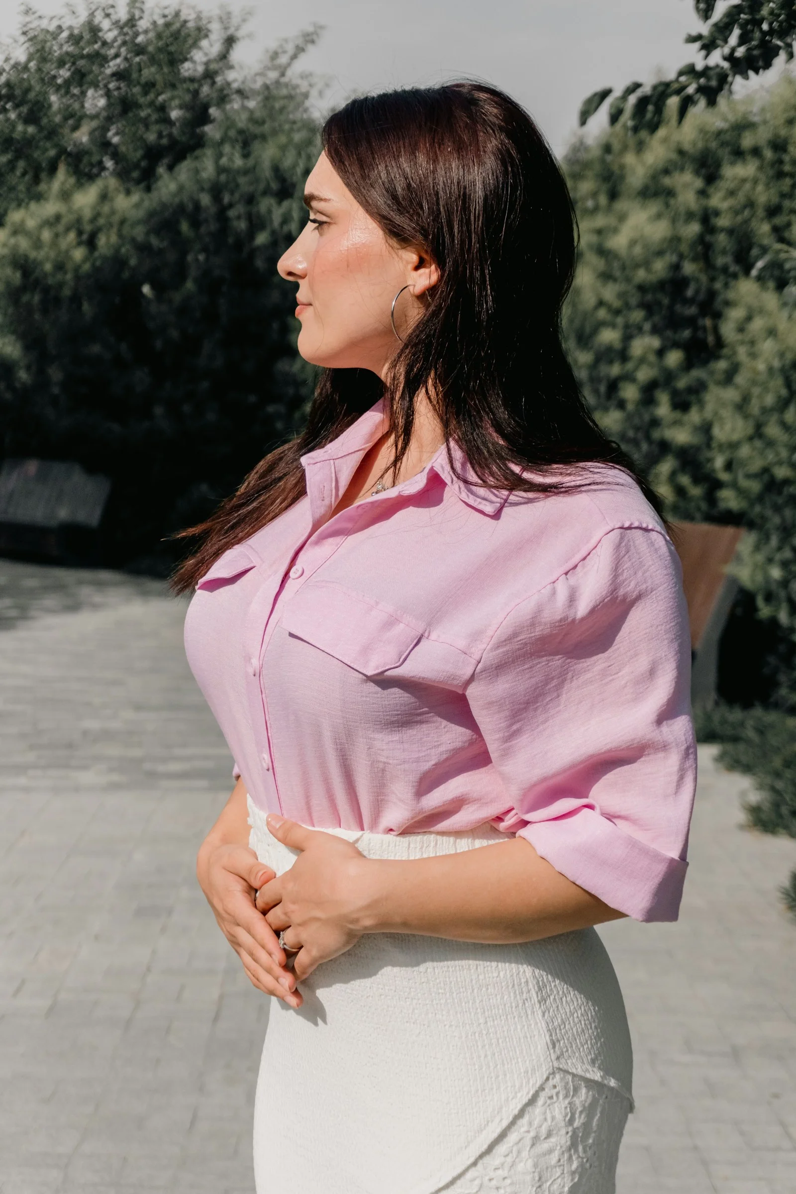 A woman in a pink button-down shirt and white skirt in a park
