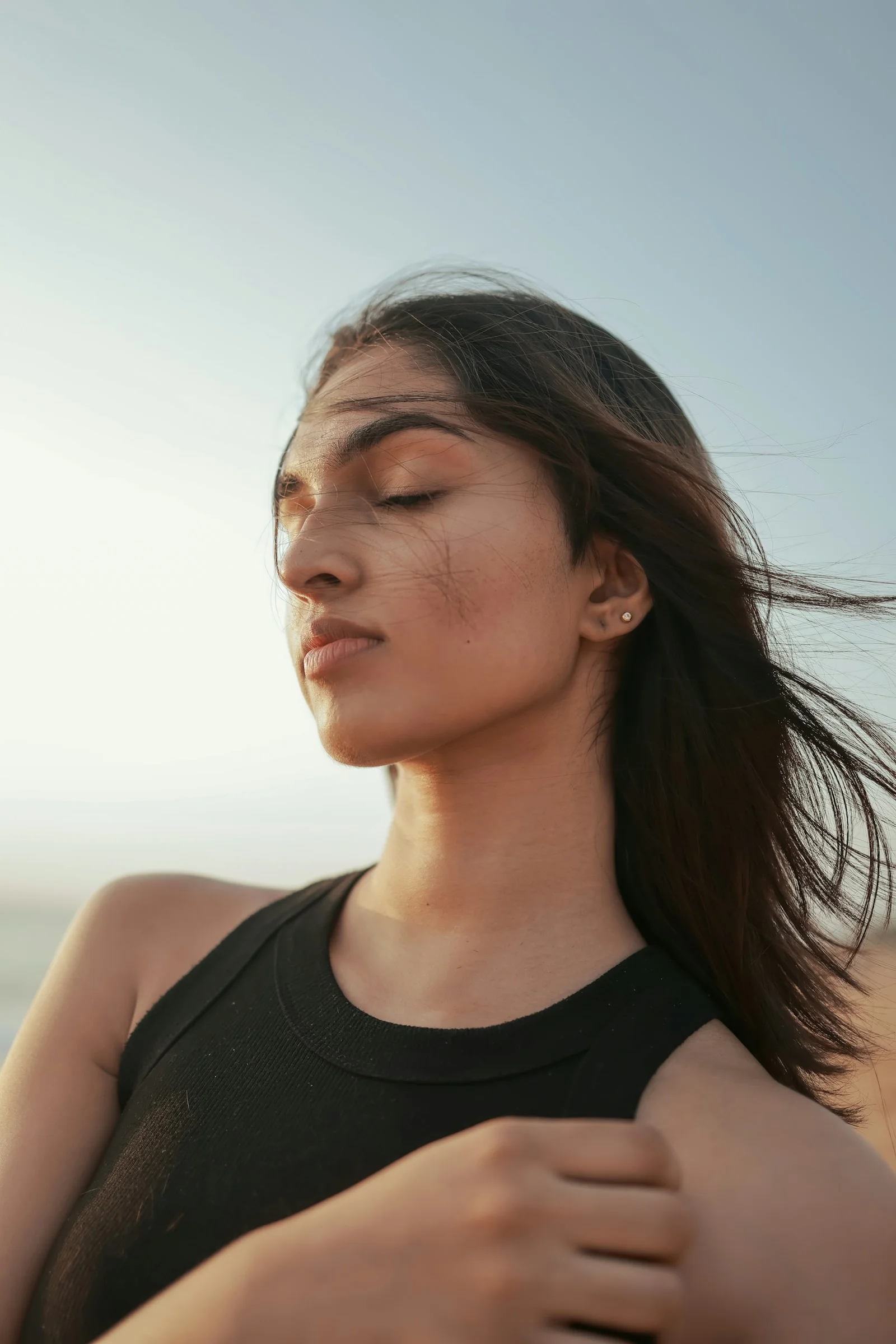A woman standing on the beach with her eyes closed