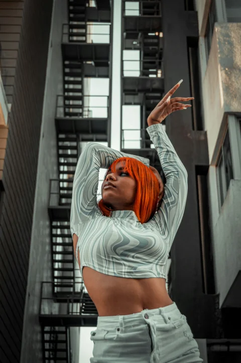 a woman with orange hair is posing in front of a building