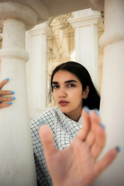 A woman with blue nails reaching toward the camera between two white stone pillars