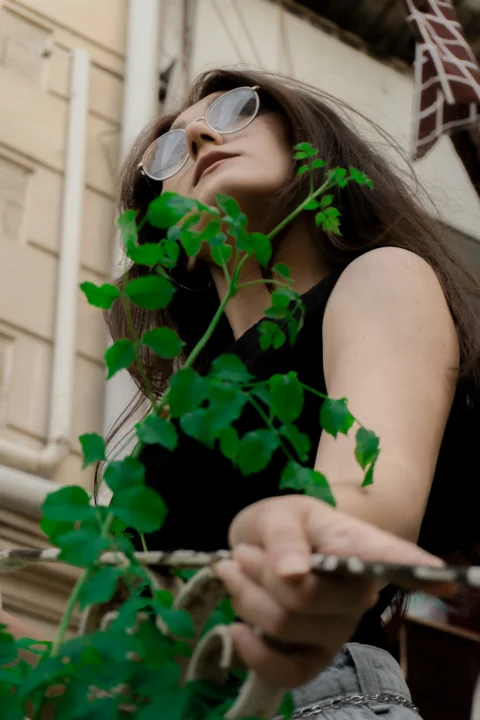 A woman with glasses holding a green plant in front of a building