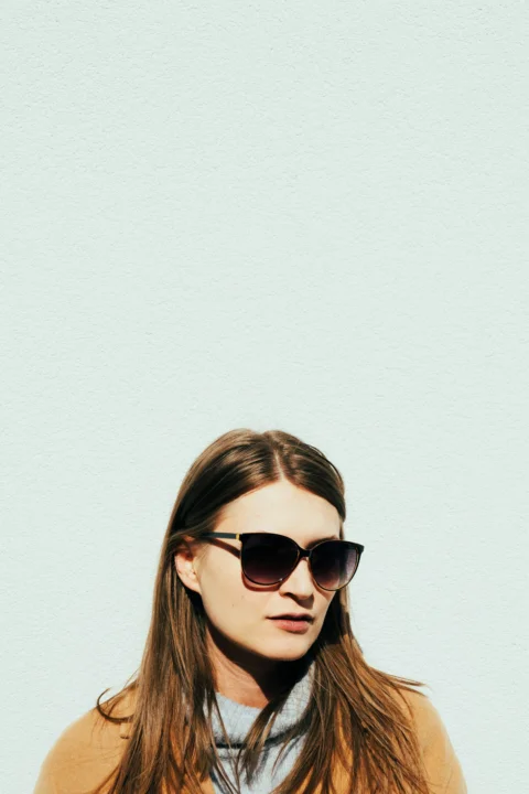a woman wearing sunglasses standing in front of a white wall