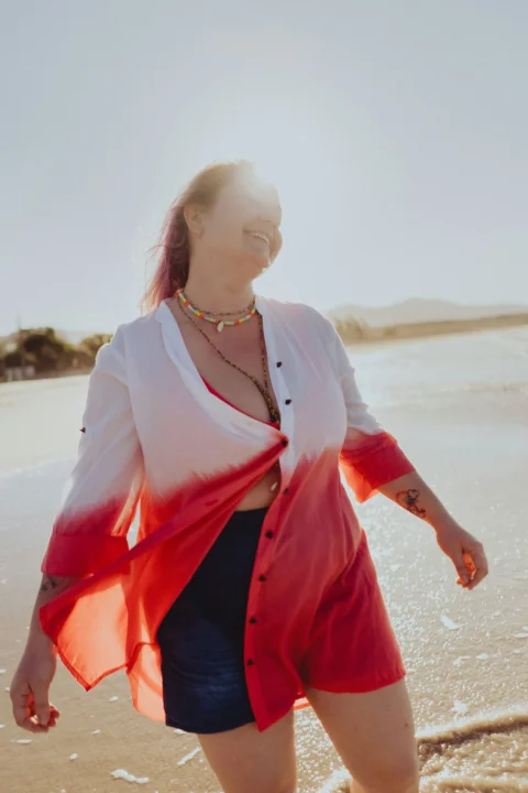 a woman in a red and white shirt is walking on the beach