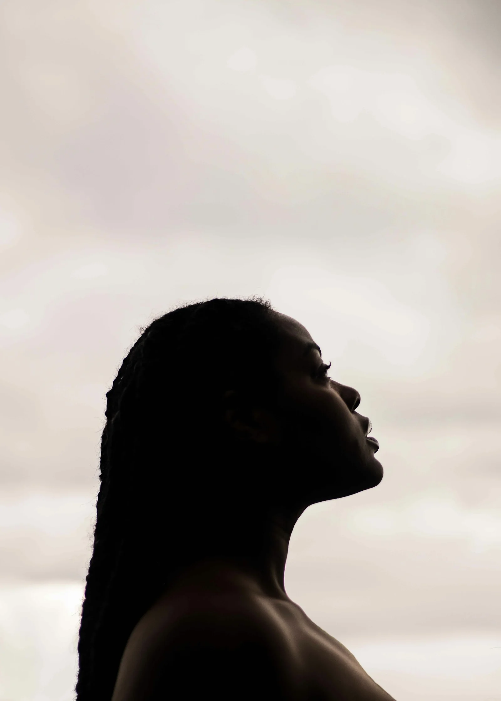 A silhouette of a woman with braided hair against a bright overcast sky