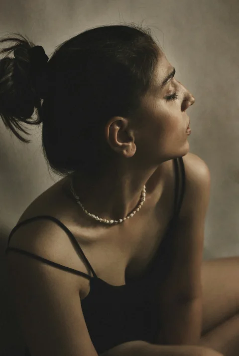 A woman with hair in a bun wearing a shell necklace