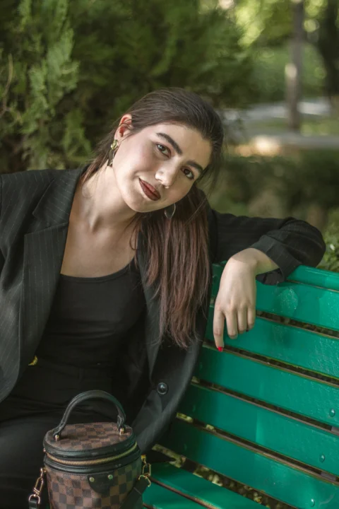 Woman in black suit sitting on a green park bench