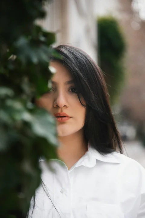 Woman peeking from behind green leaves