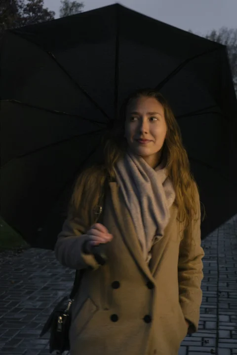 a woman holding a black umbrella on a sidewalk