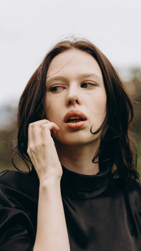 Young woman in black top looking sideways, hand near face