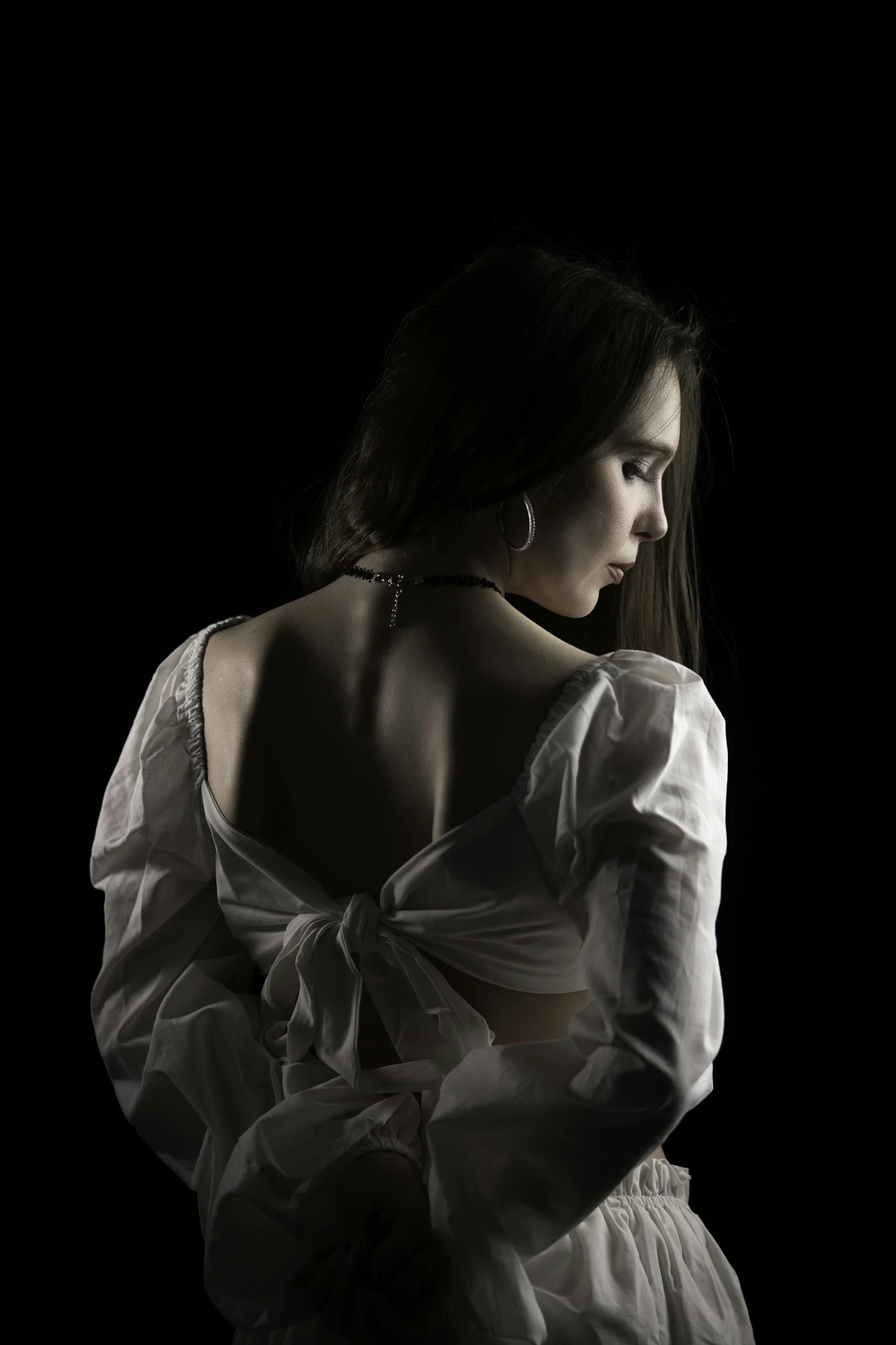 A woman in a white blouse with a tied back against a black background